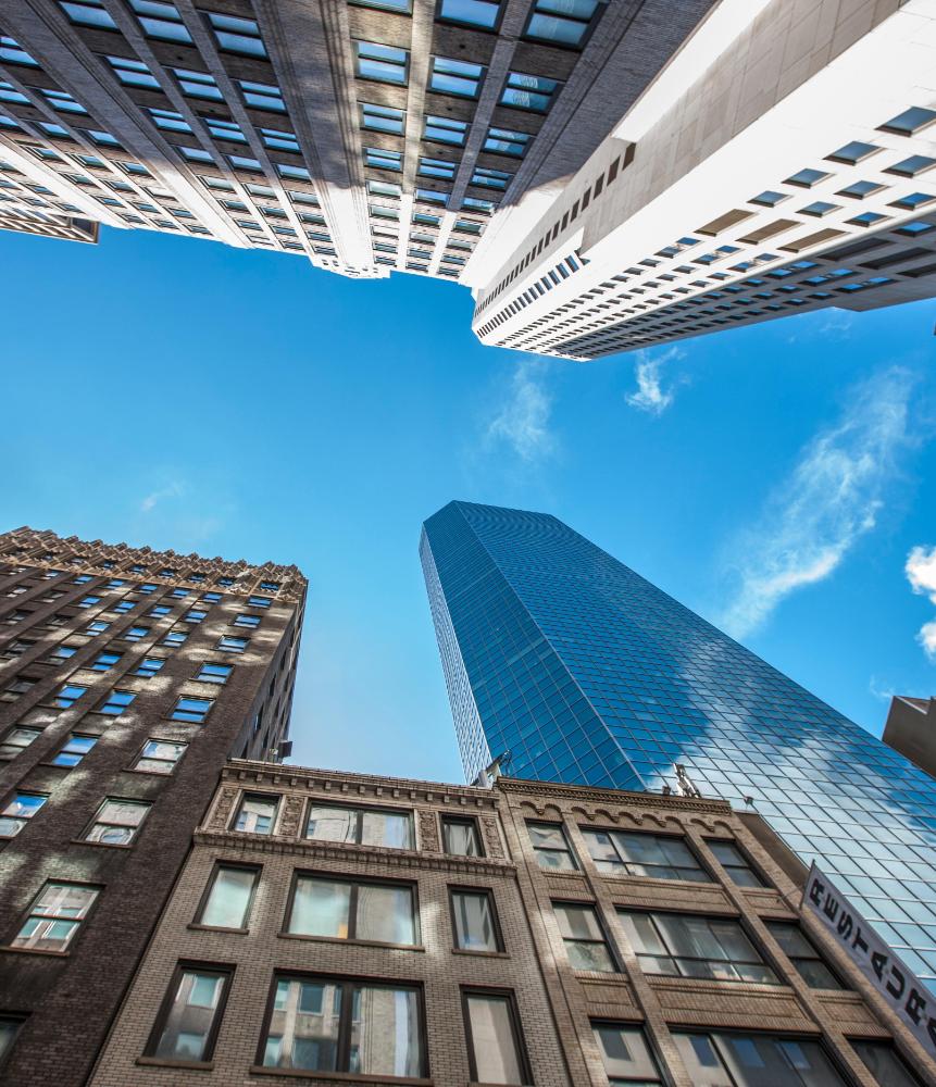 Low-angle view of modern glass tower surrounded by historic urban buildings, reflecting mixed-era city real estate investment.